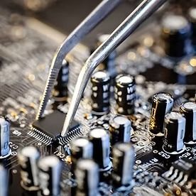 Tweezers placing a microchip on a circuit board, close-up with electronic components.