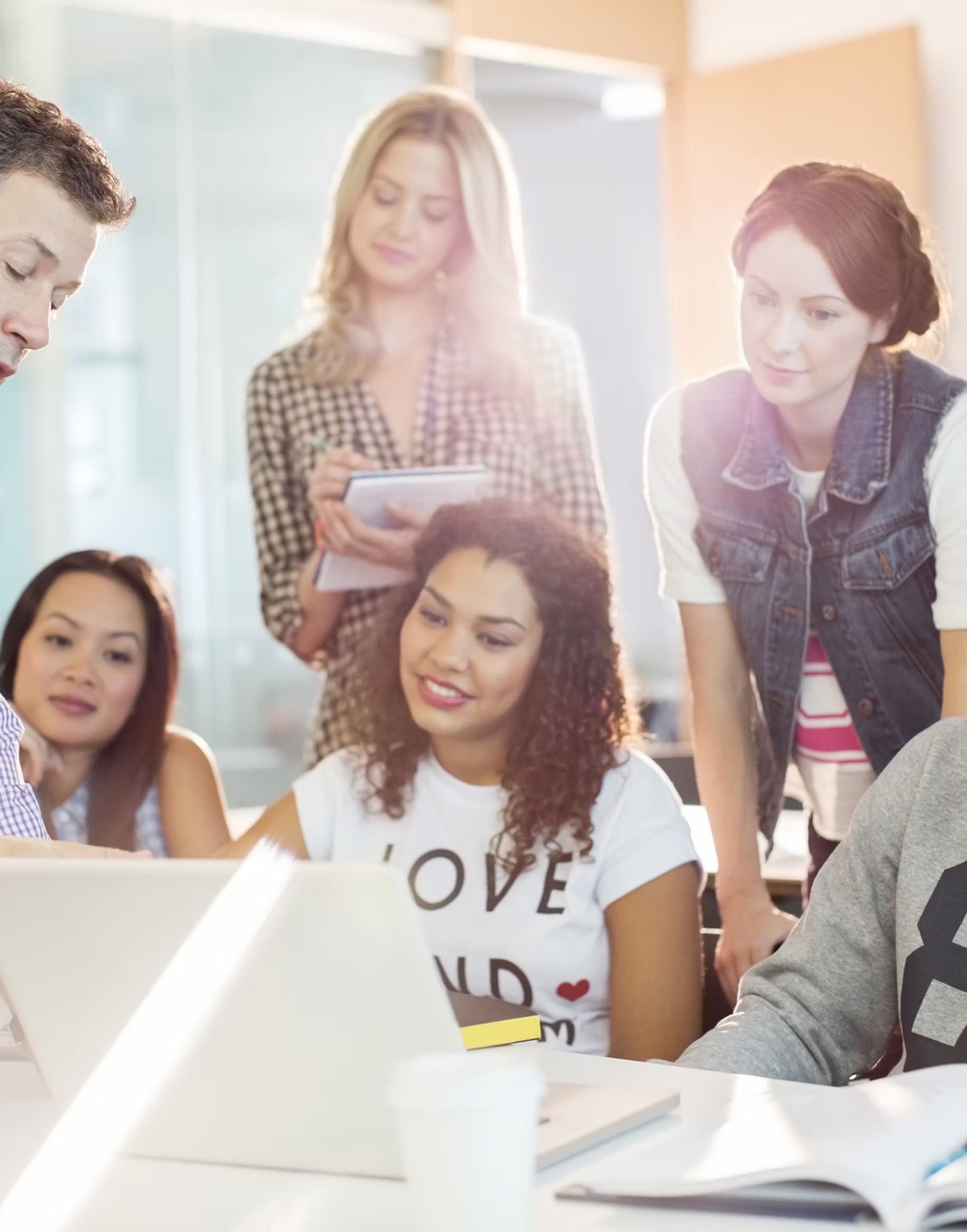 Group of people collaborating around laptops in a brightly lit office setting.