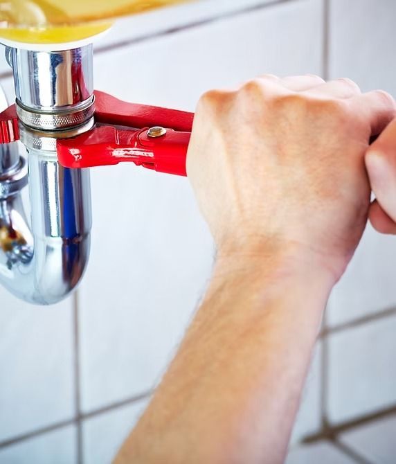 Hand using red wrench on chrome pipe under sink.