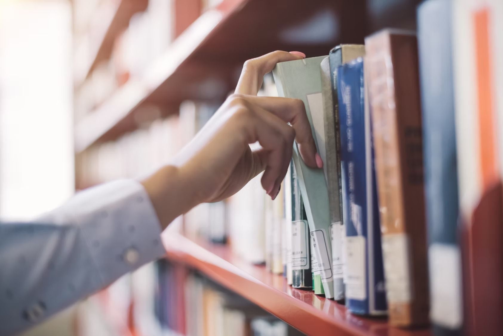 Hand reaching for a book on a shelf in a library.