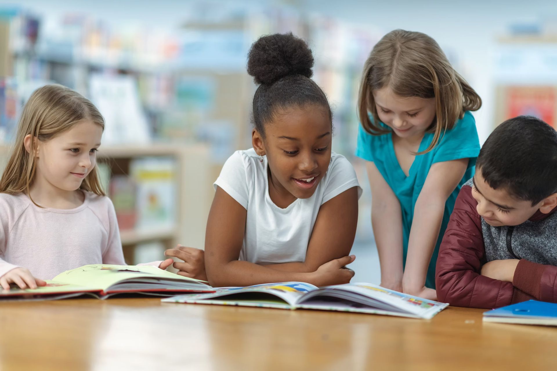 Four children reading books together at a table in a library.
