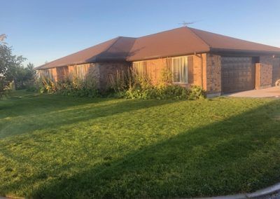 A brick house with a brown roof and a large lawn in front of it.