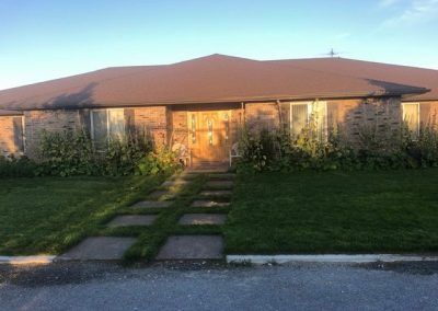 A brick house with a brown roof and a lush green lawn in front of it.
