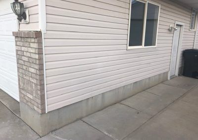 A white house with a brick pillar and a concrete walkway.