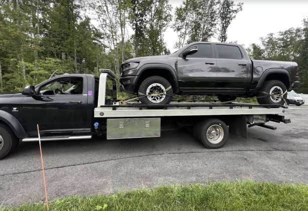 A black truck is being towed by a tow truck.