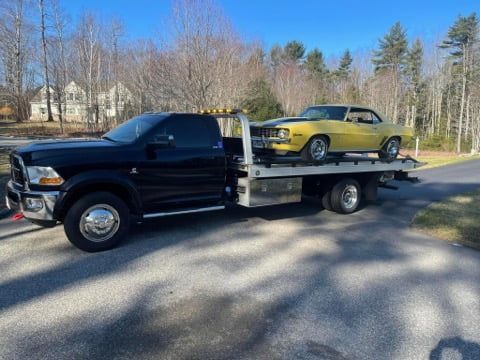 A black tow truck is towing a yellow car.