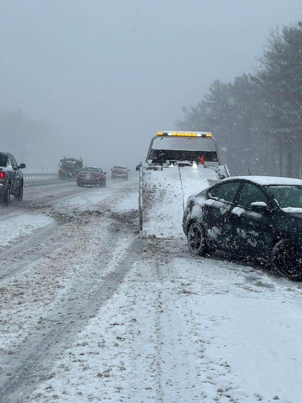 A tow truck is pulling a car out of the snow on a snowy road.