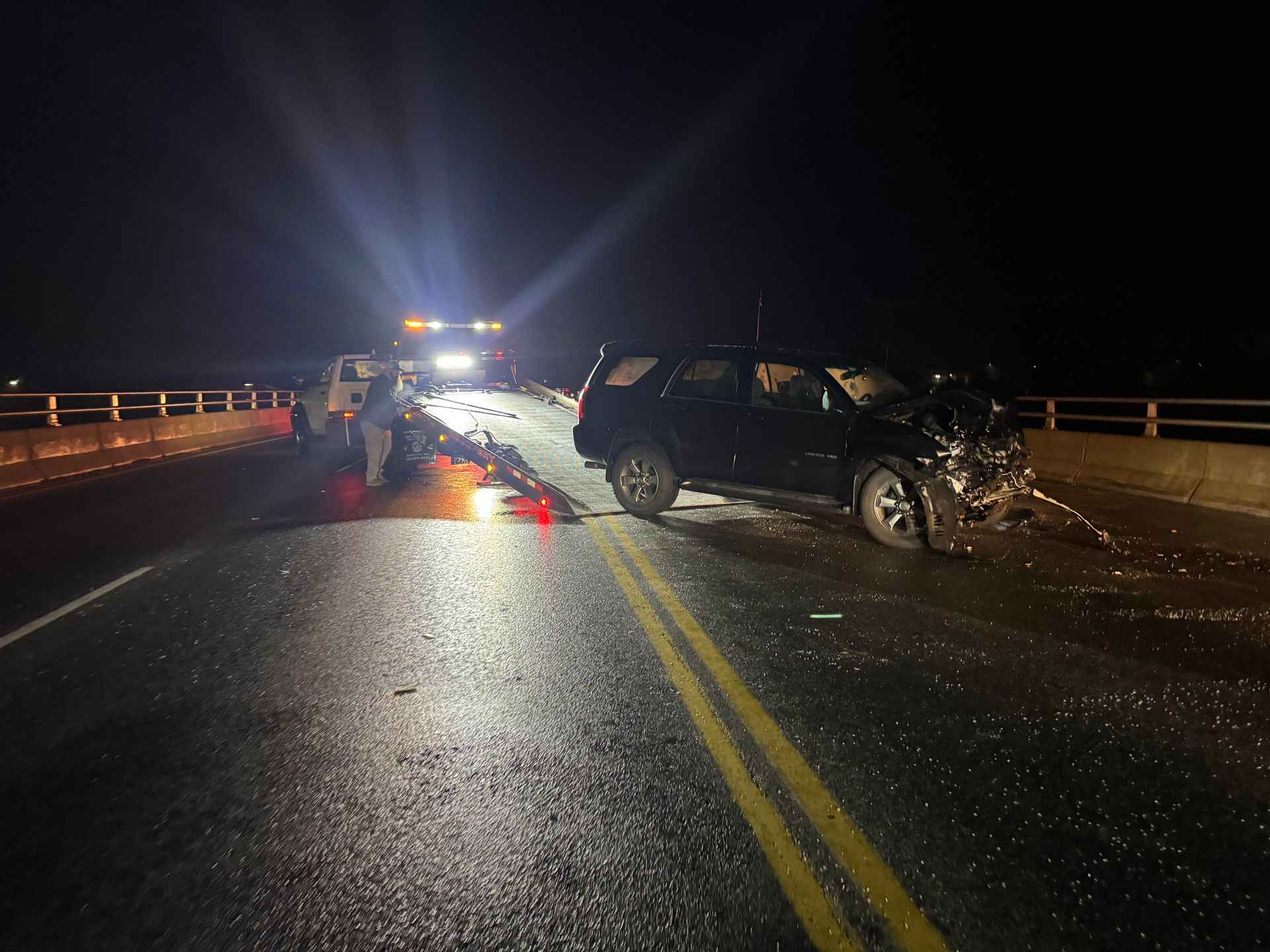 A car is sitting on the side of the road next to a tow truck.