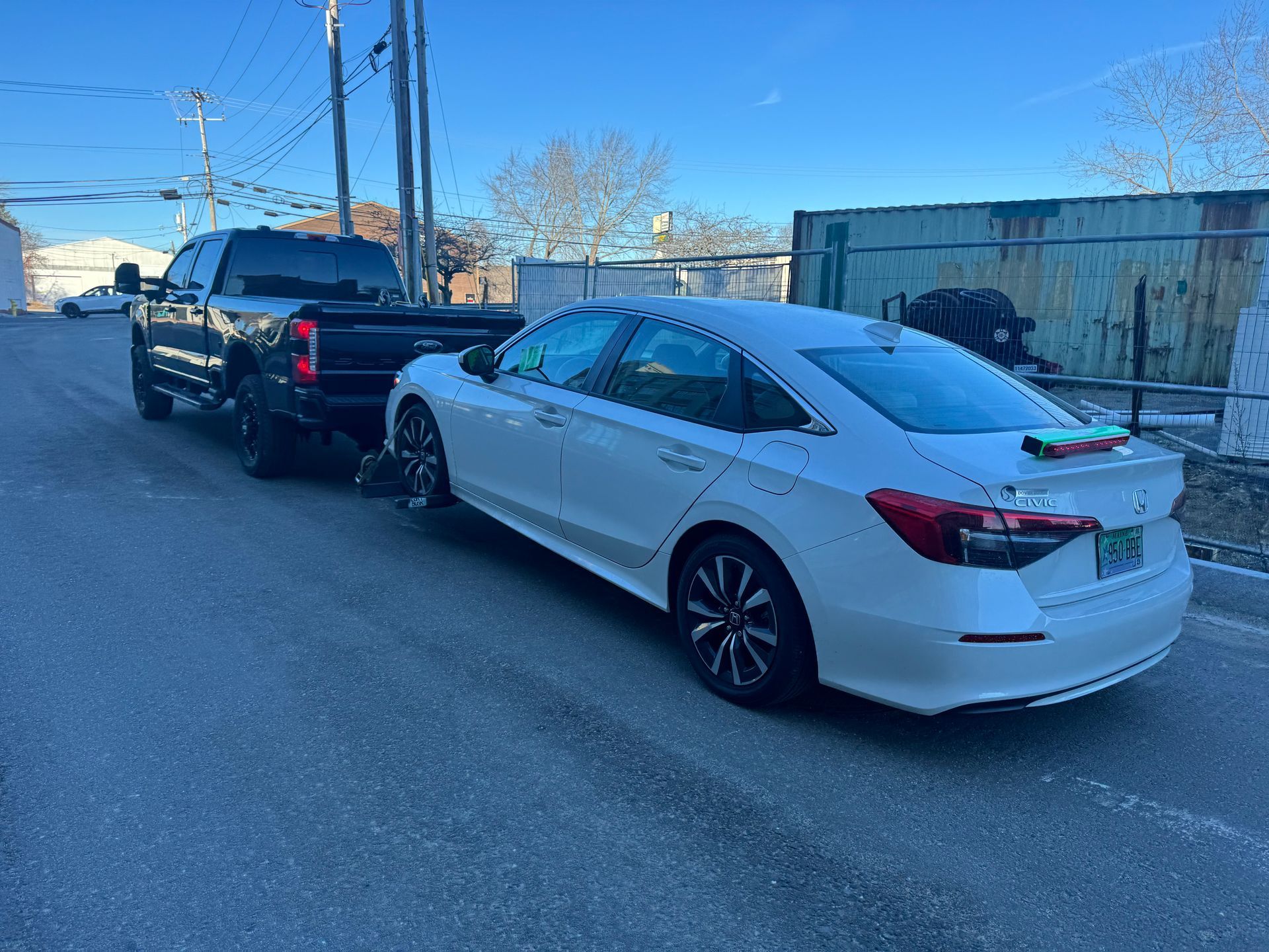 A white car is being towed by a black truck.