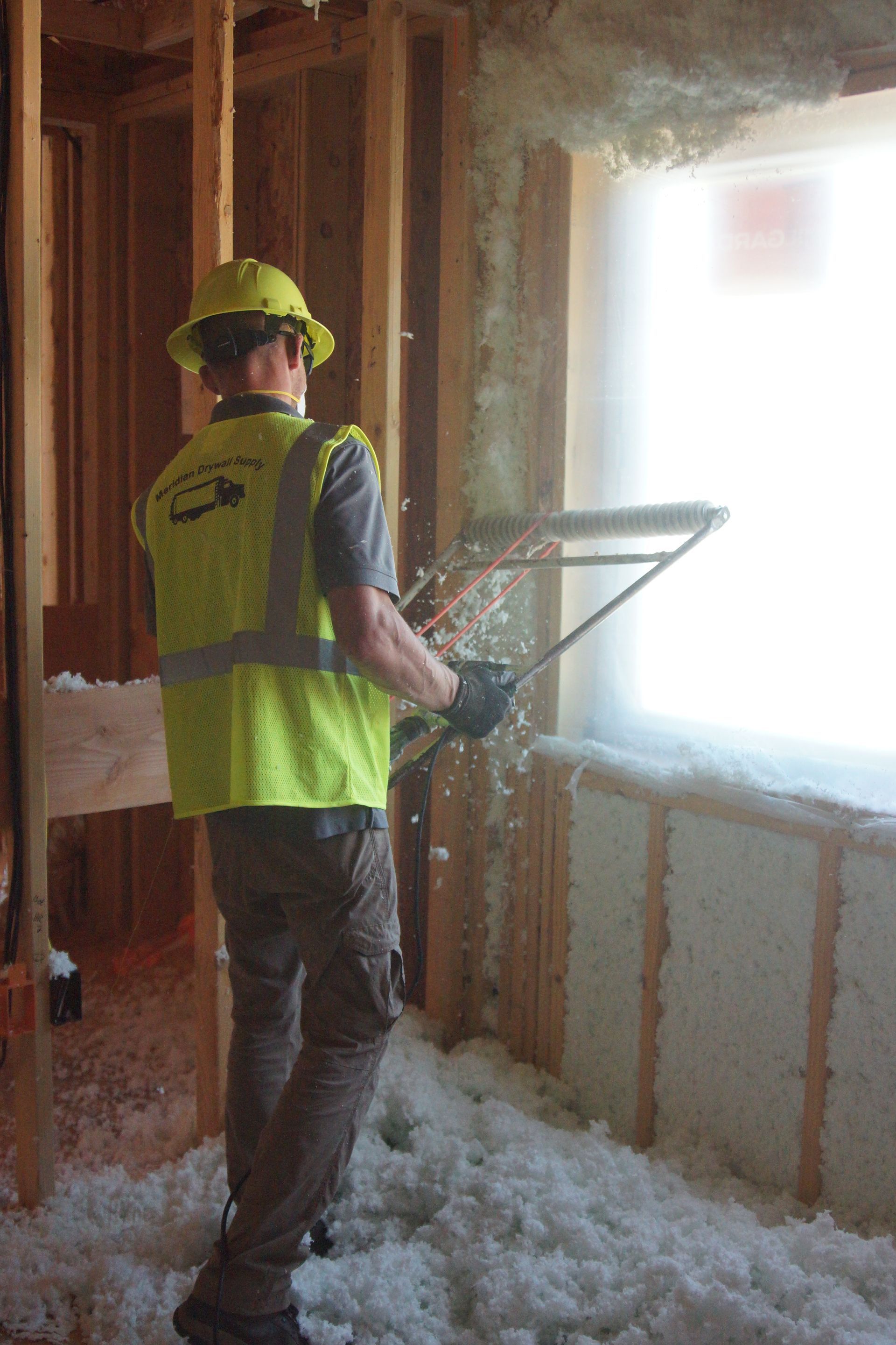 Construction worker installing insulation inside a wall, wearing a hard hat and safety vest.