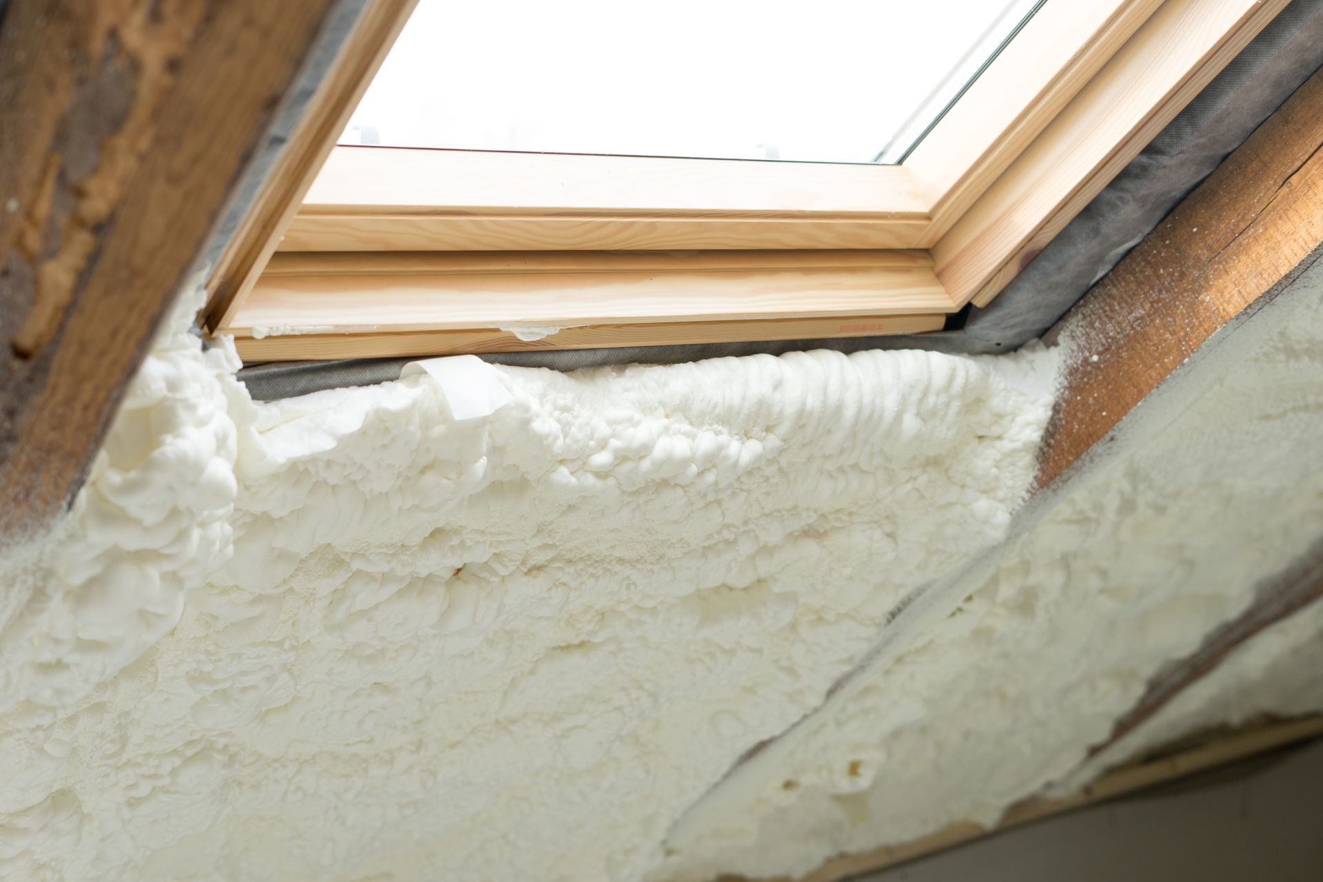 White spray foam insulation around a skylight in a wooden frame.