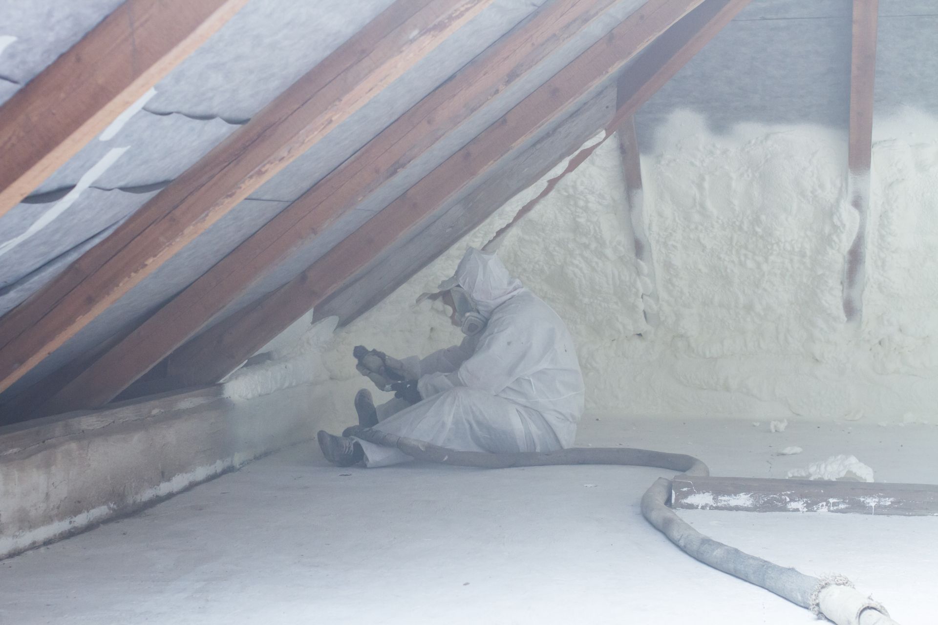 Person in protective suit spraying foam insulation in an attic.