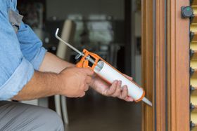 Person caulking a wooden door frame with a caulk gun.
