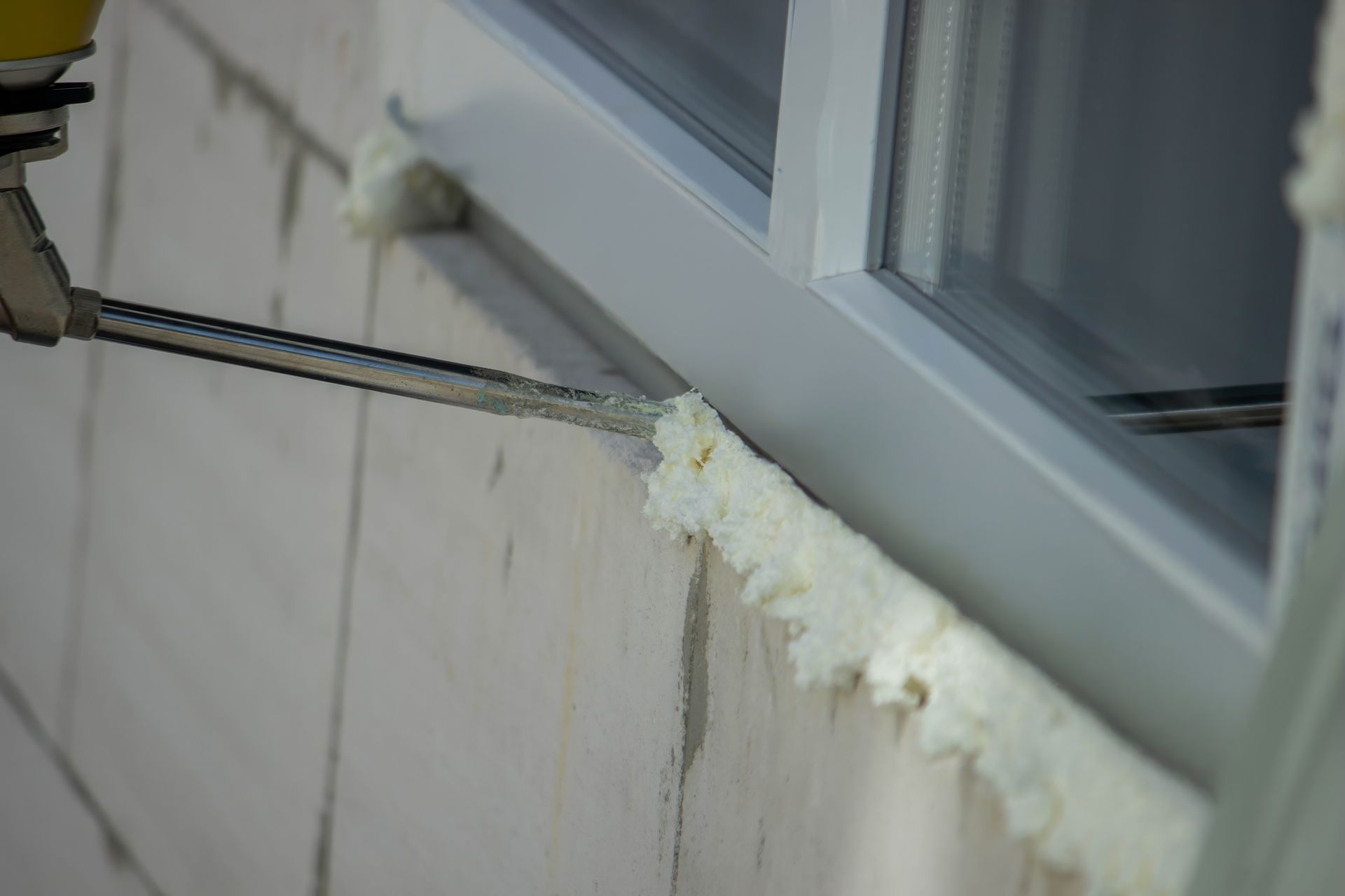 Person sealing a window frame with expanding foam, on a white brick building.