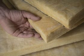 Hand holding a piece of yellow insulation, stacked with more pieces in a close-up shot.