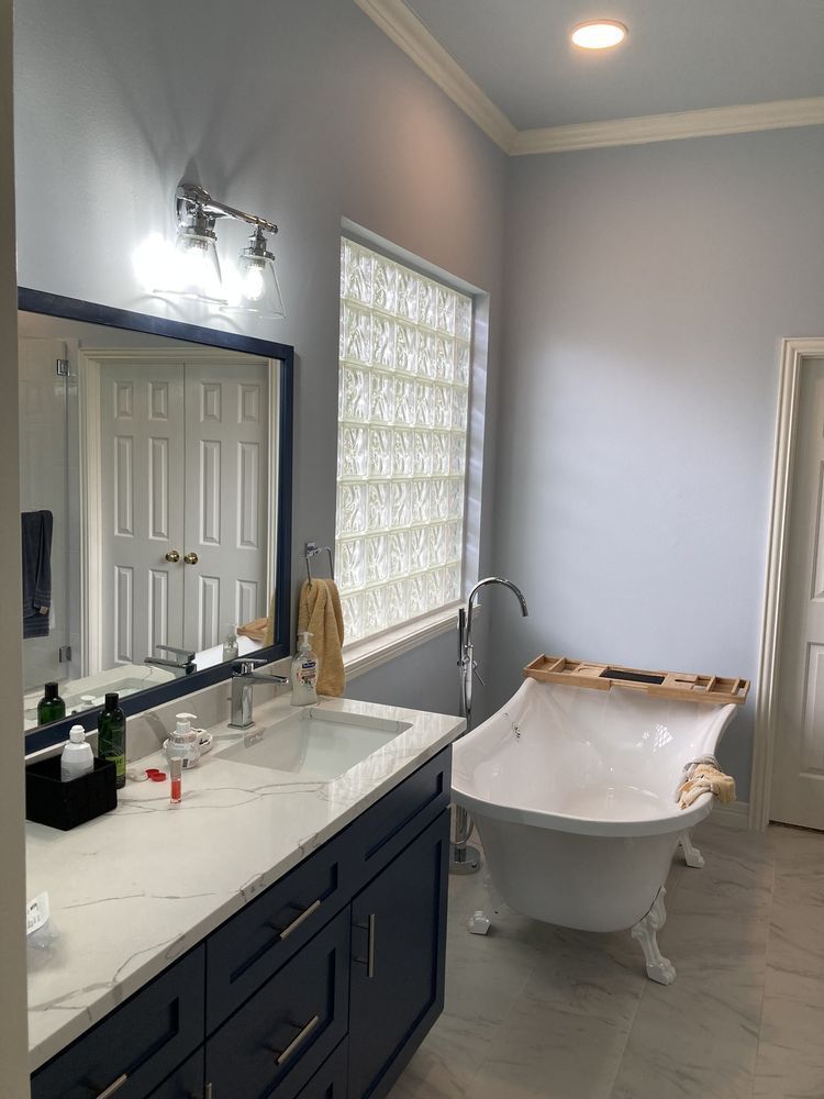 A bathroom with a tub , sink , mirror and window.