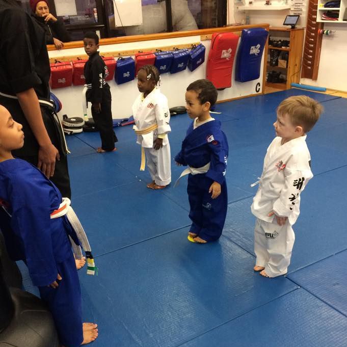 a group of kids in karate uniforms are standing on a blue mat