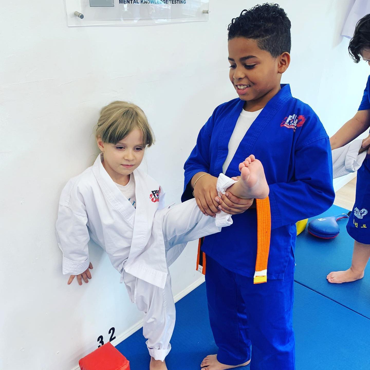 a boy in a blue karate uniform stretches his leg