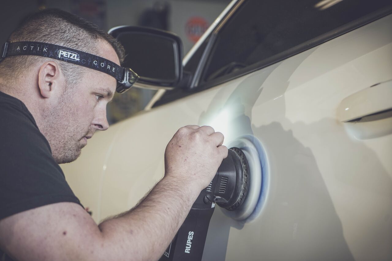A man is polishing the side mirror of a car.