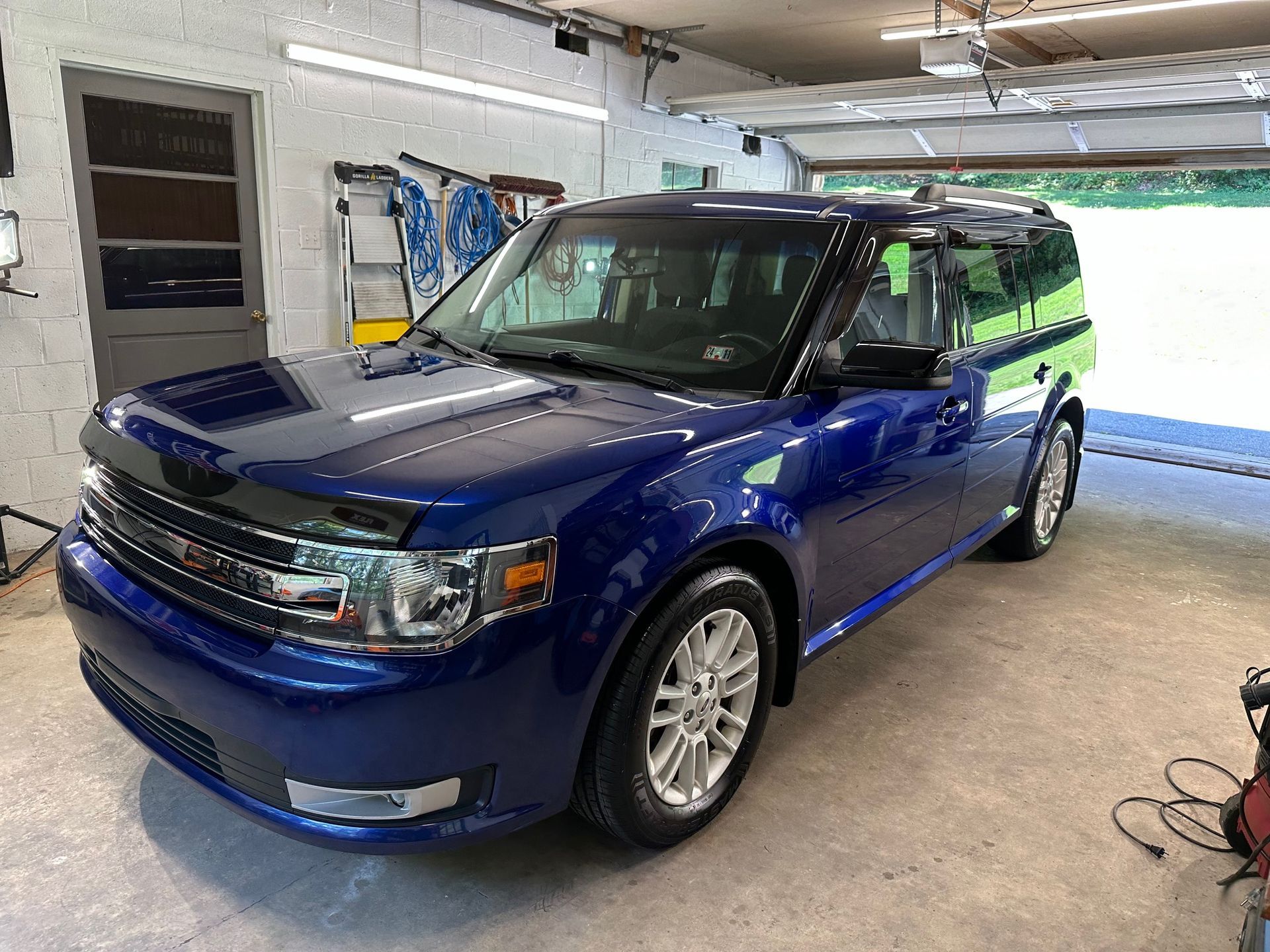 A blue ford flex is parked in a garage.