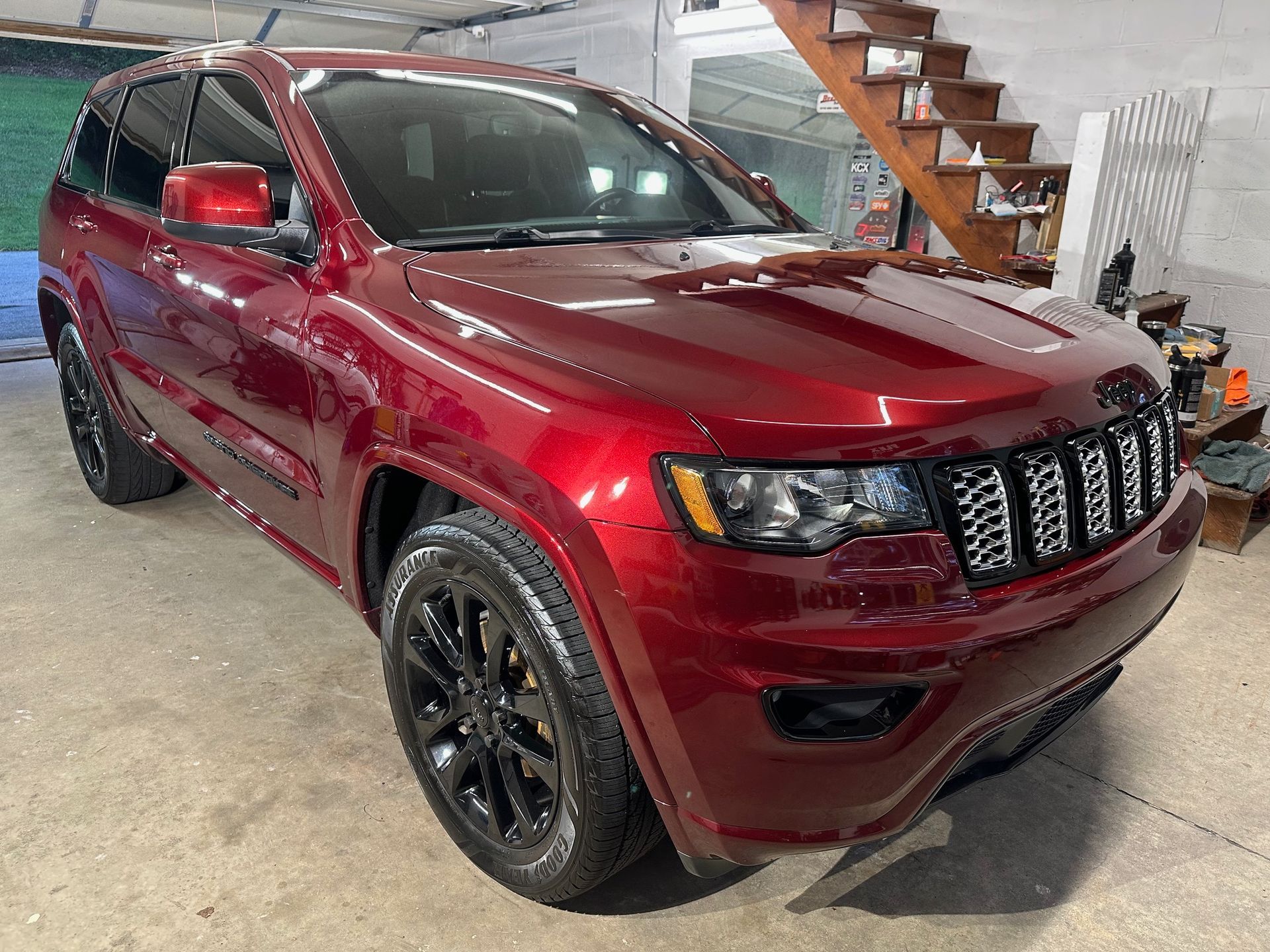 A red jeep grand cherokee is parked in a garage next to a staircase.