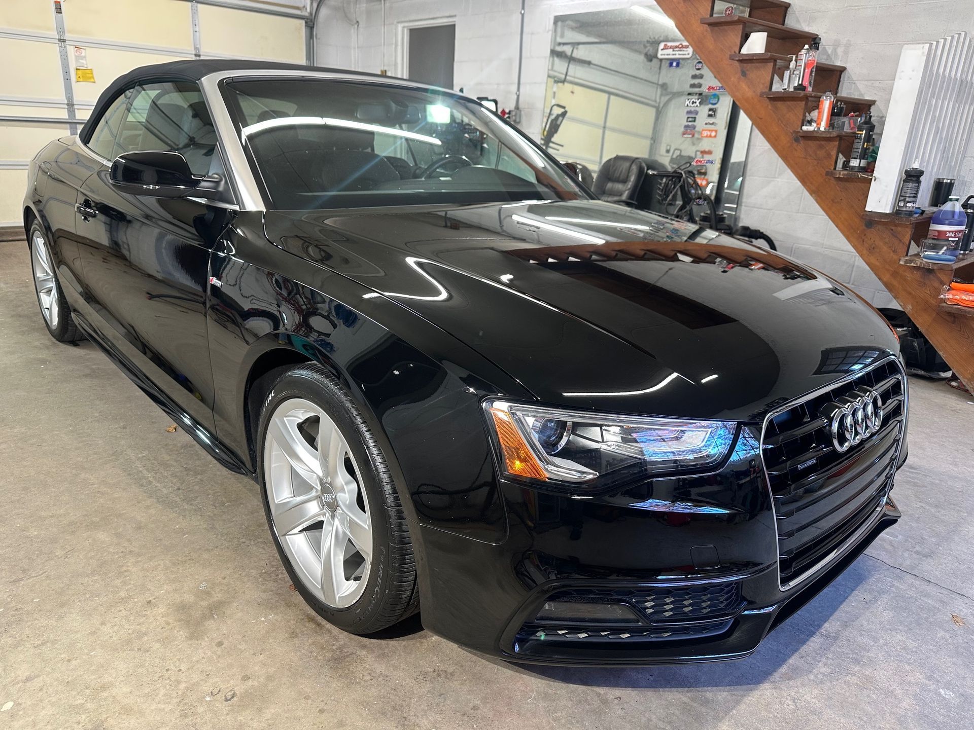 A black audi a5 convertible is parked in a garage next to a staircase.