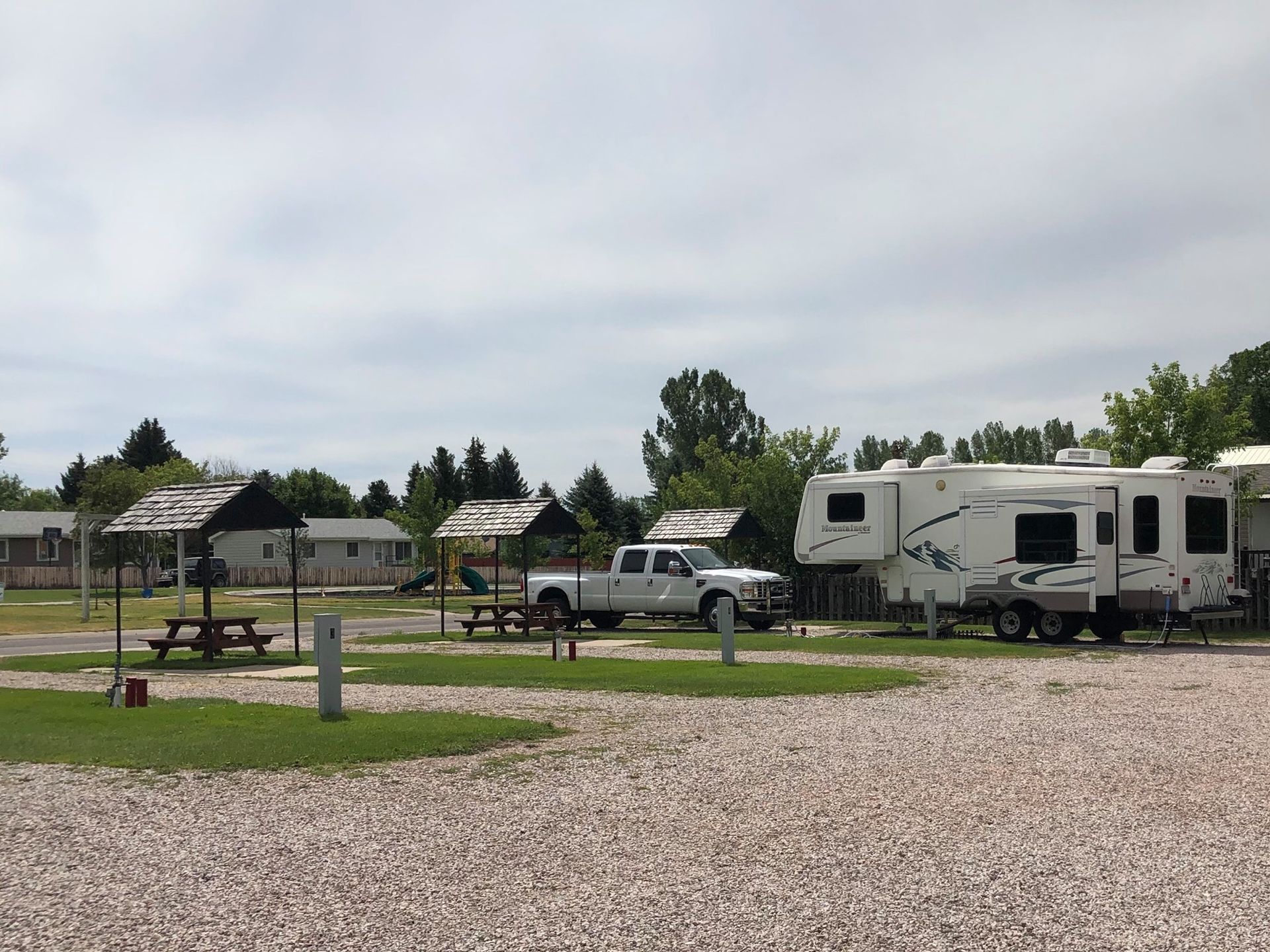 A white truck is parked in a gravel lot next to a rv.