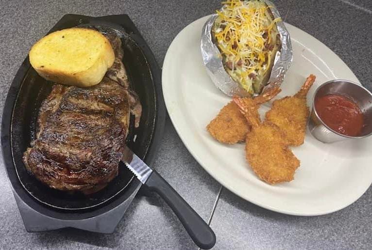 steak with garlic bread, baked potato and shrimp with cocktail sauce