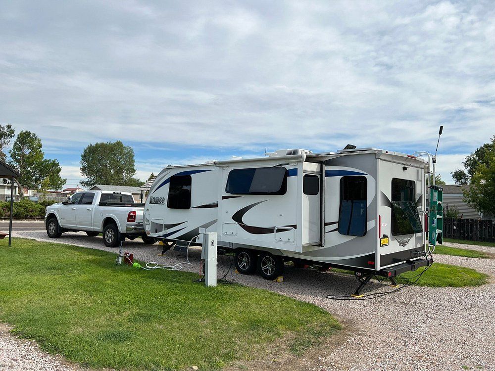 A rv is parked in a gravel lot next to a truck.