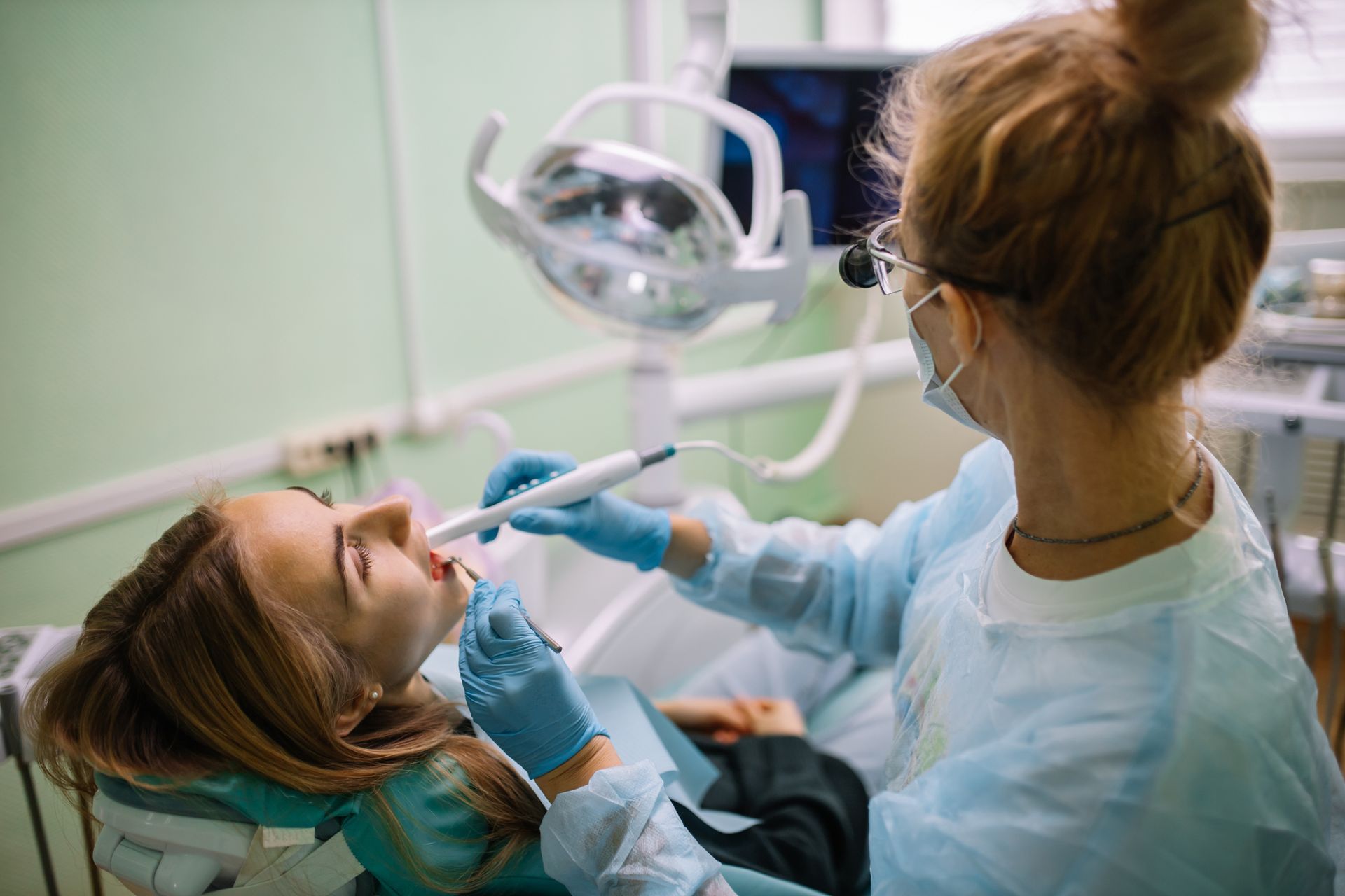 A female patient sitting in a chair with her mouth open as an emergency dentist conduct examination.