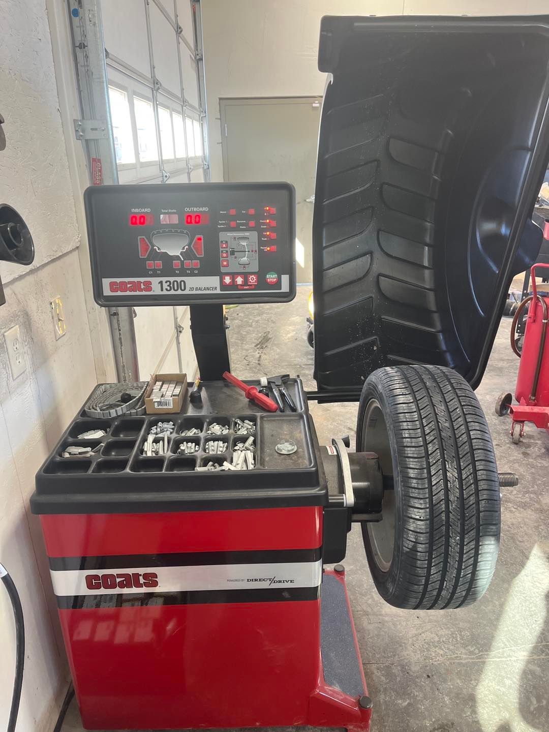 A tire balancing machine is sitting next to a tire in a garage.