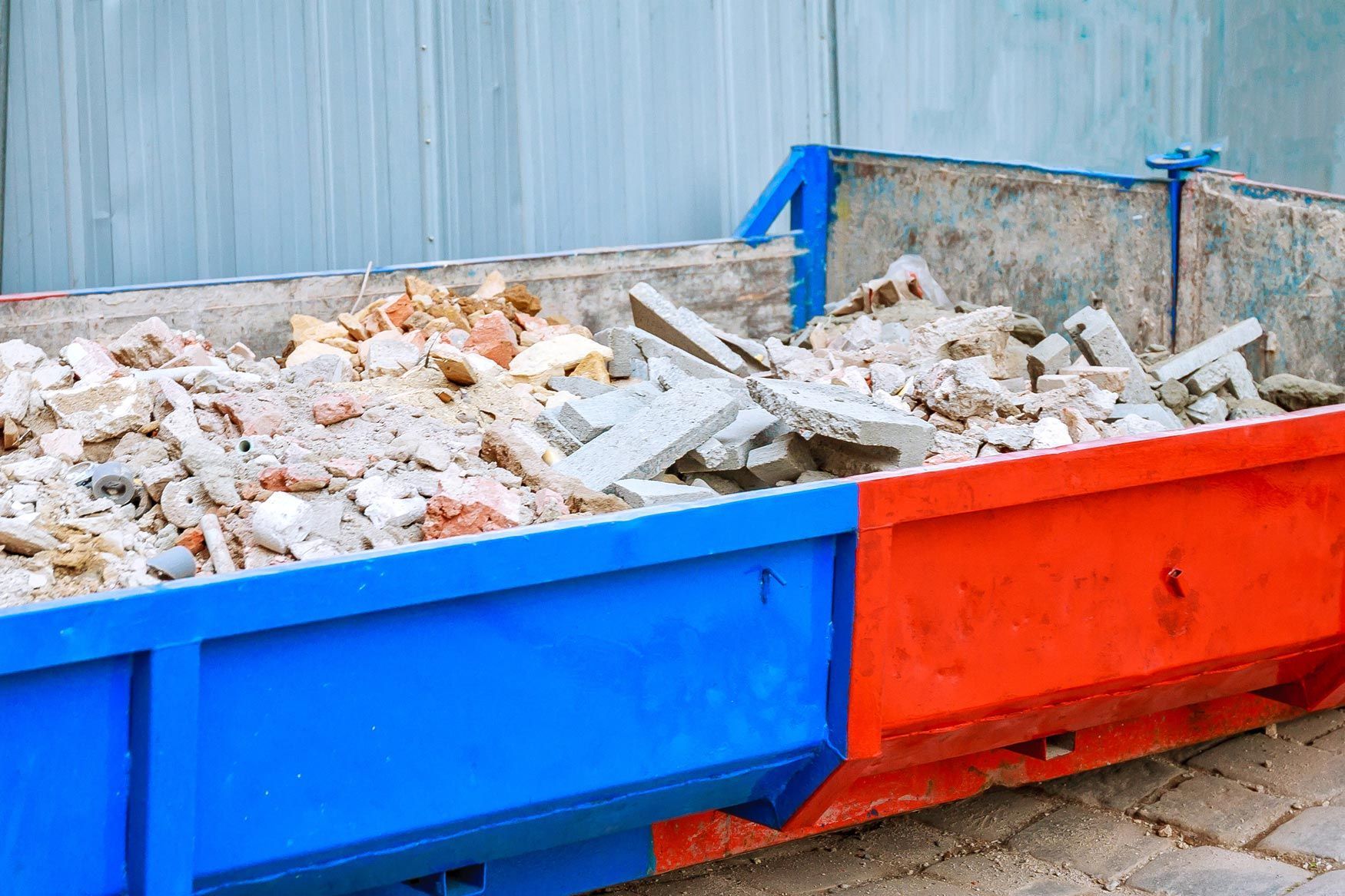 Blue and red dumpster filled with construction debris, outdoors.