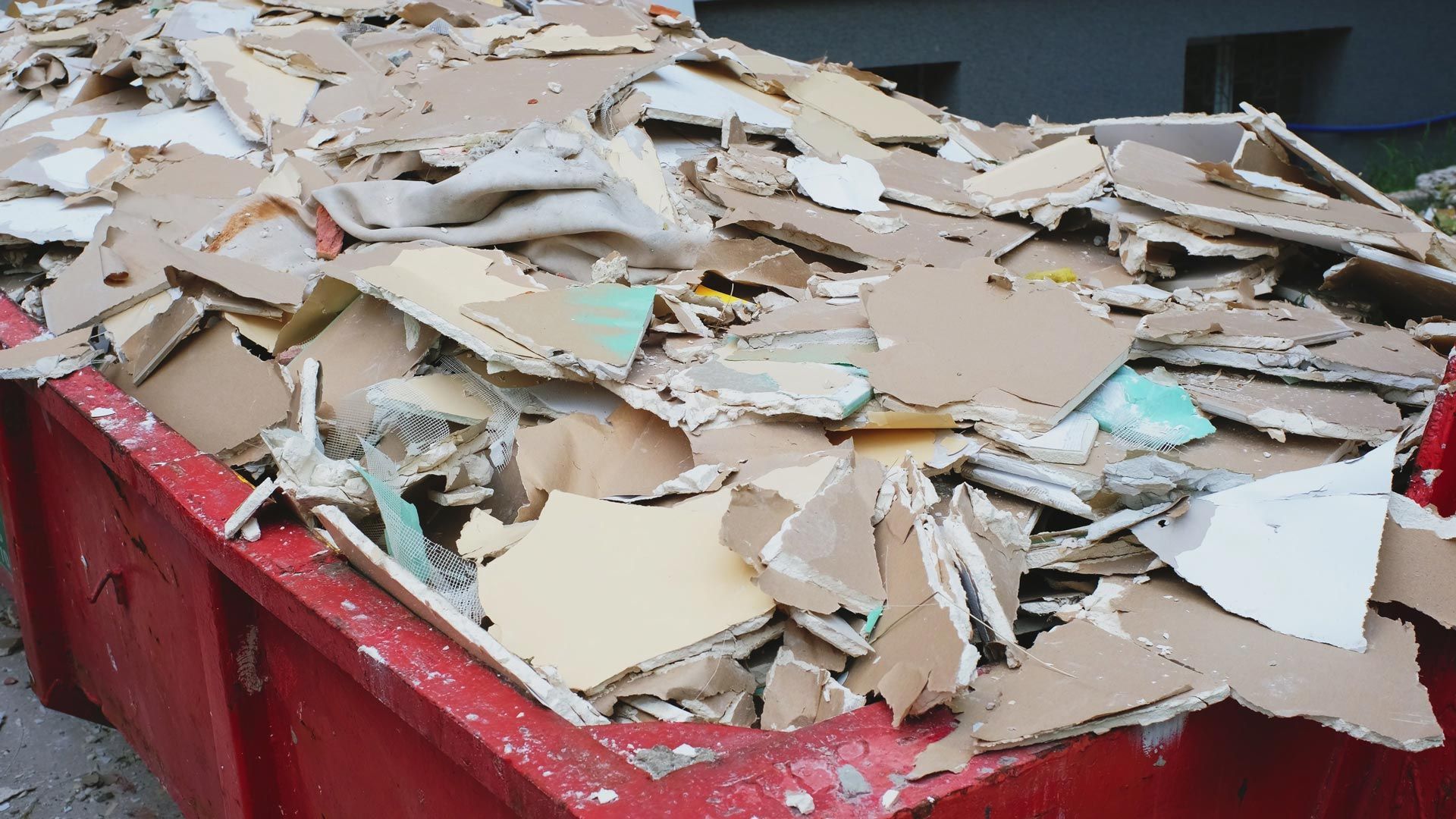 Red dumpster filled with torn drywall pieces.