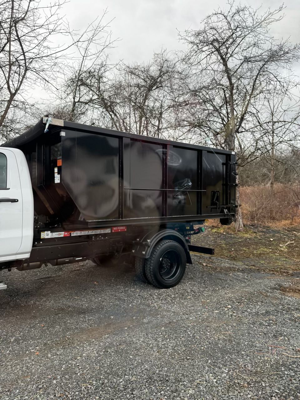 Blue dumpster on a driveway next to a building and greenery.