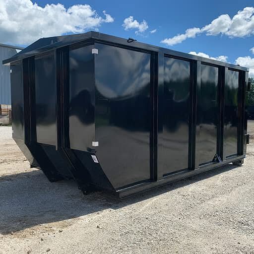 Blue dumpster on a residential street next to trash cans and a wooden fence.