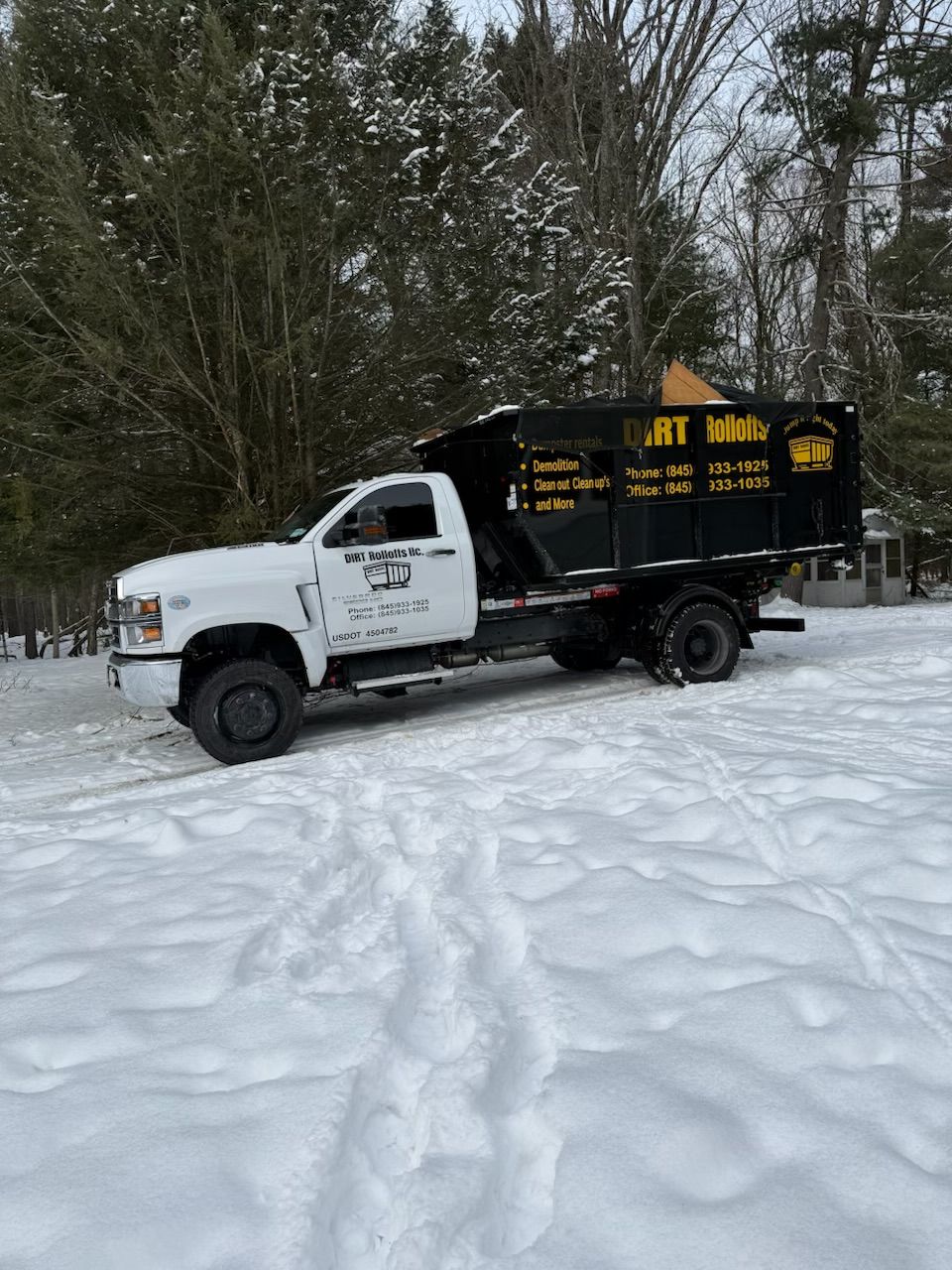 Orange excavator loading debris into a dump truck on a road.