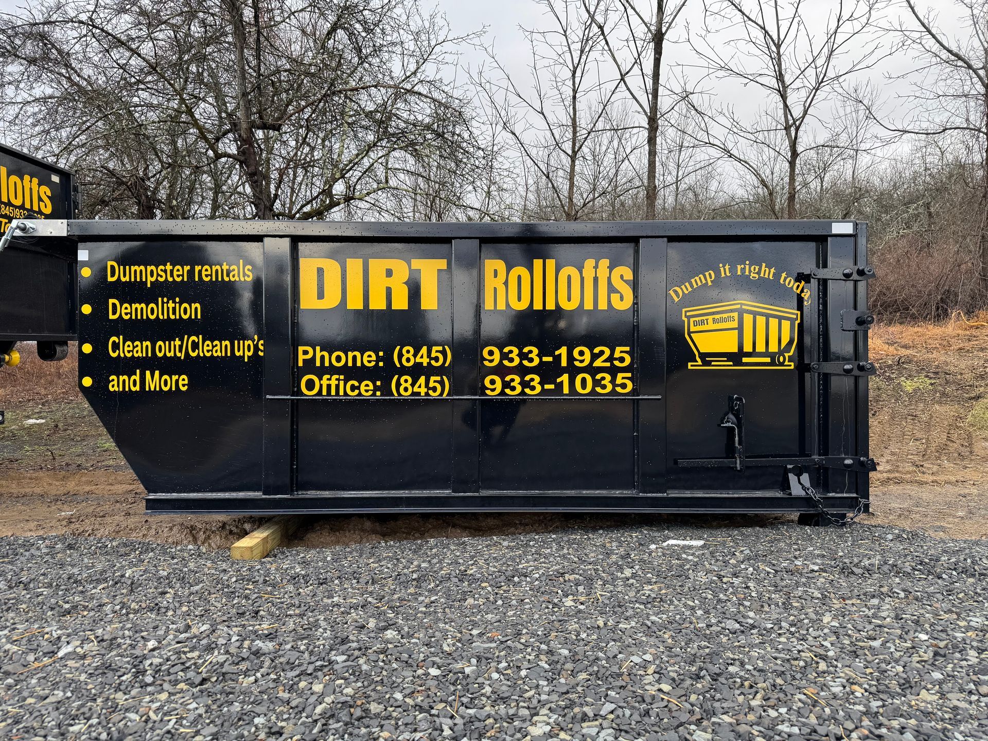 Black dumpster on green grass with trees in background.