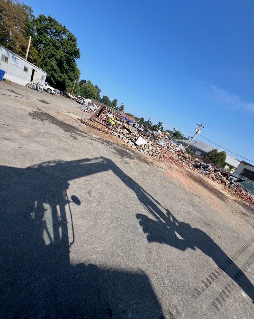 Black dump trailer on gravel in front of a blue sky, power lines, and trees.