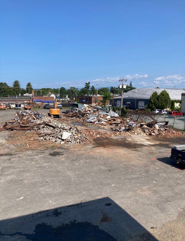 Demolished building rubble piles in a parking lot on a sunny day.