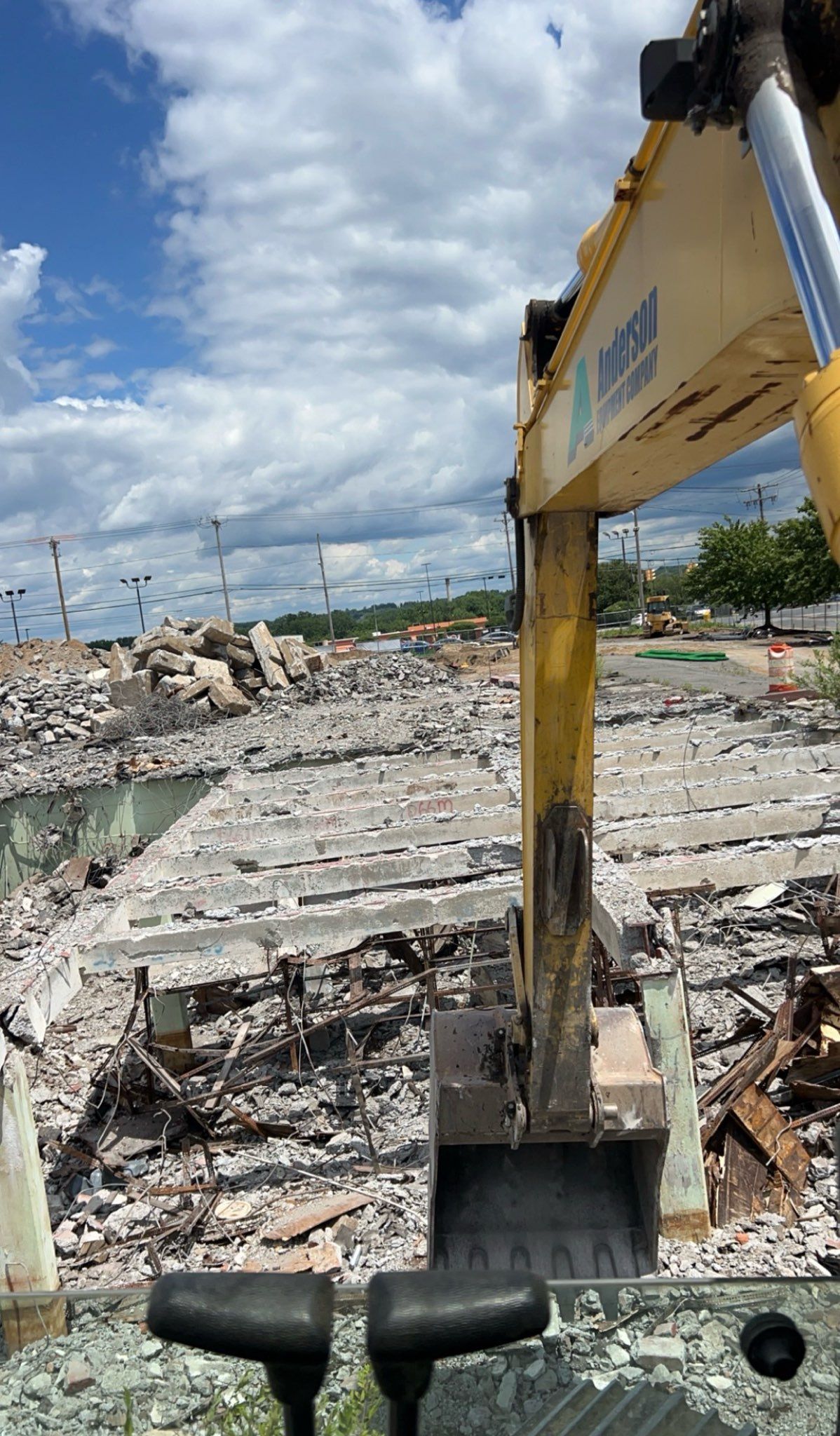 Excavator demolishing concrete structure under a partly cloudy sky.