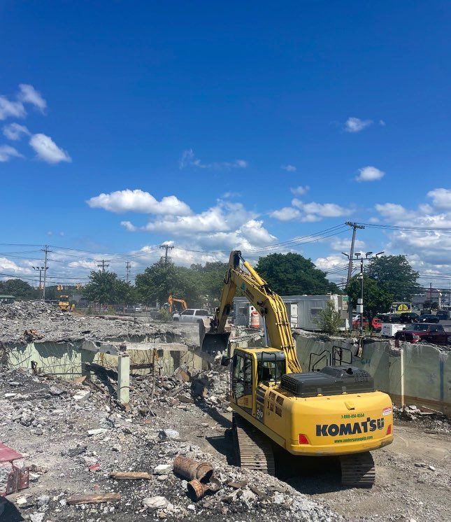 Excavator demolishing concrete structure under a partly cloudy sky.