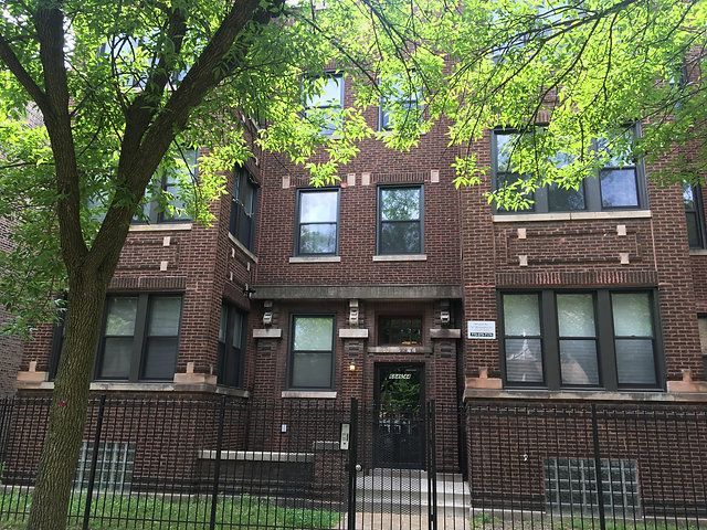 A brick apartment building with a fence around it and trees in front of it.