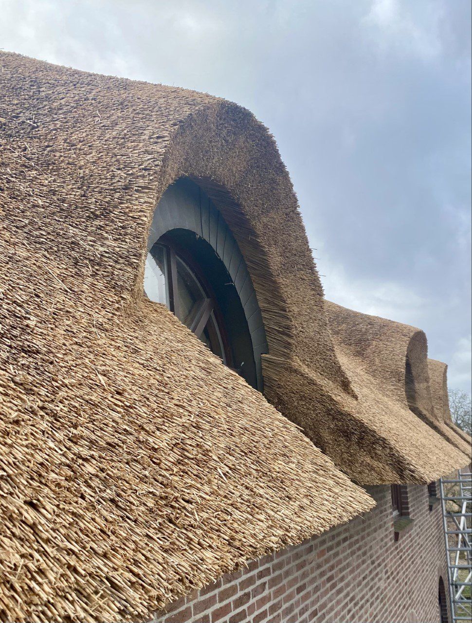 Een bakstenen gebouw met een rieten dak en een raam.