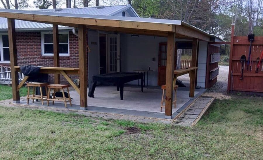 A covered patio with a concrete floor, featuring a table, stools, and ramp.