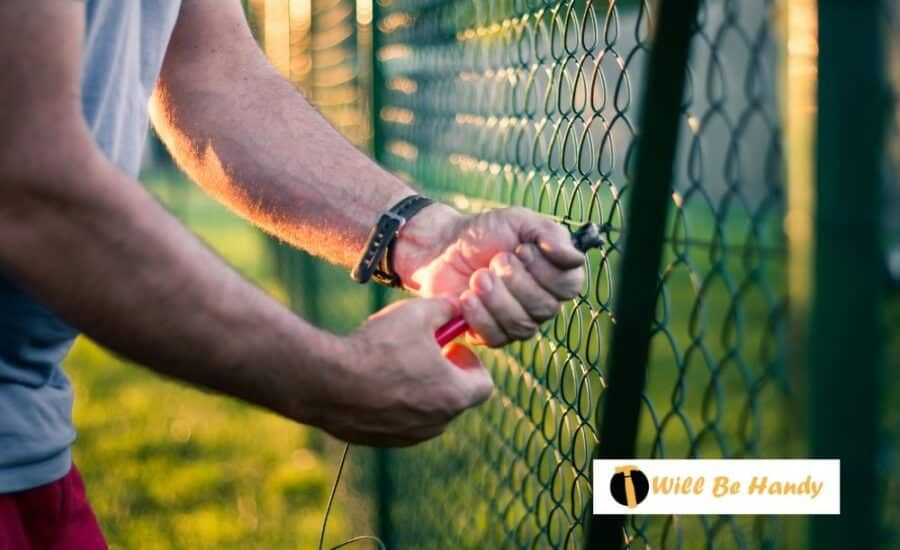 Person fixing chain-link fence with wire. Focus on hands, setting sun.