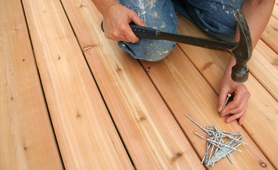 Person hammering a nail into wooden deck.
