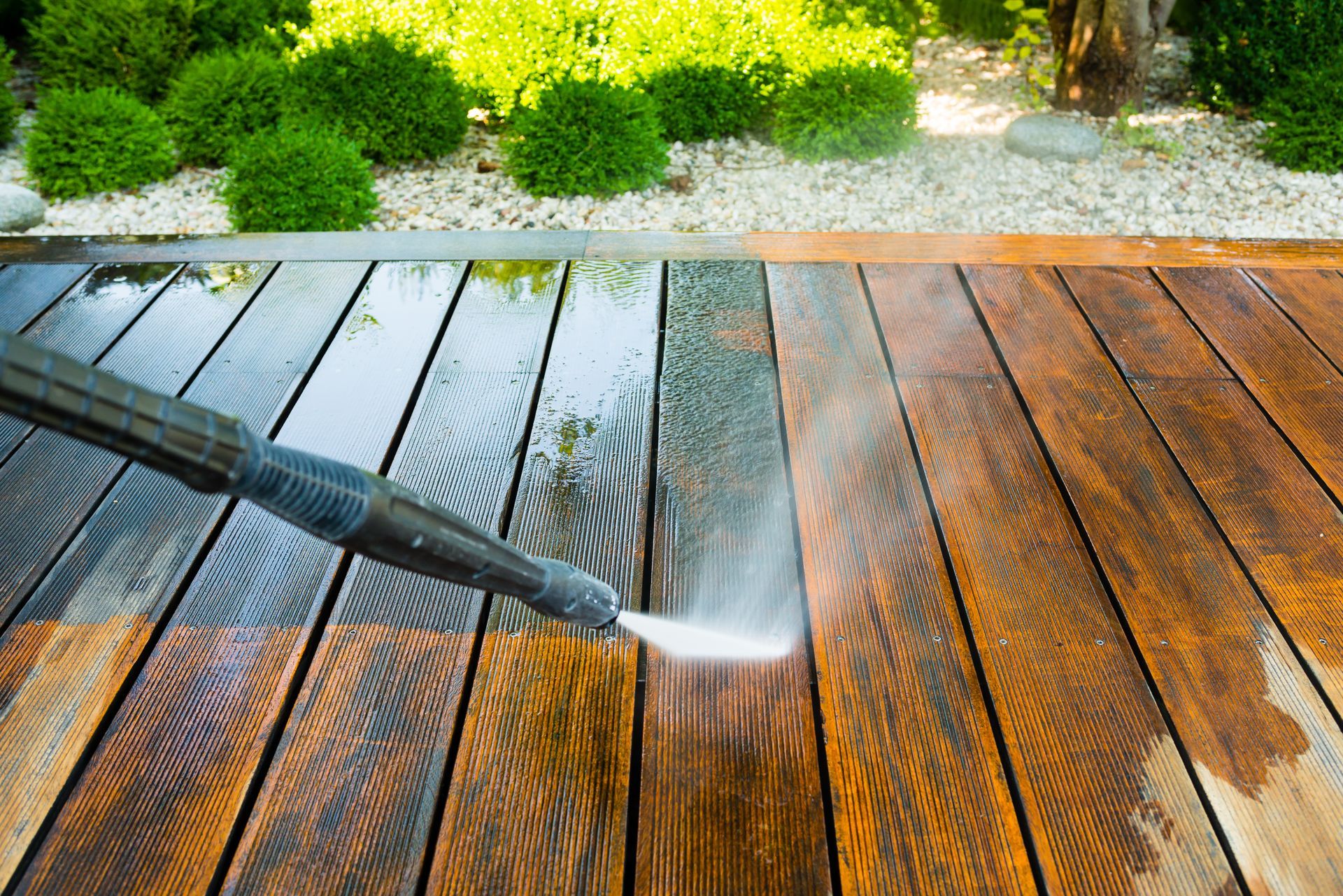 A handyman cleaning a wooden terrace with a power washer, using a high water pressure cleaner to remove dirt and grime from the surface.