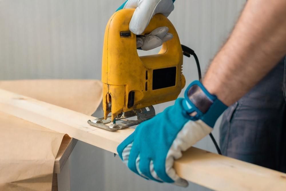 A man is using a jigsaw to cut a piece of wood.