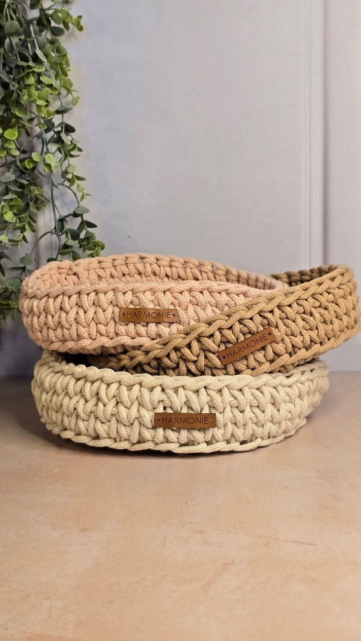 Dos cestas apiladas y tejidas a mano en crochet, una de color beige y otra de color tostado, con etiquetas de cuero.