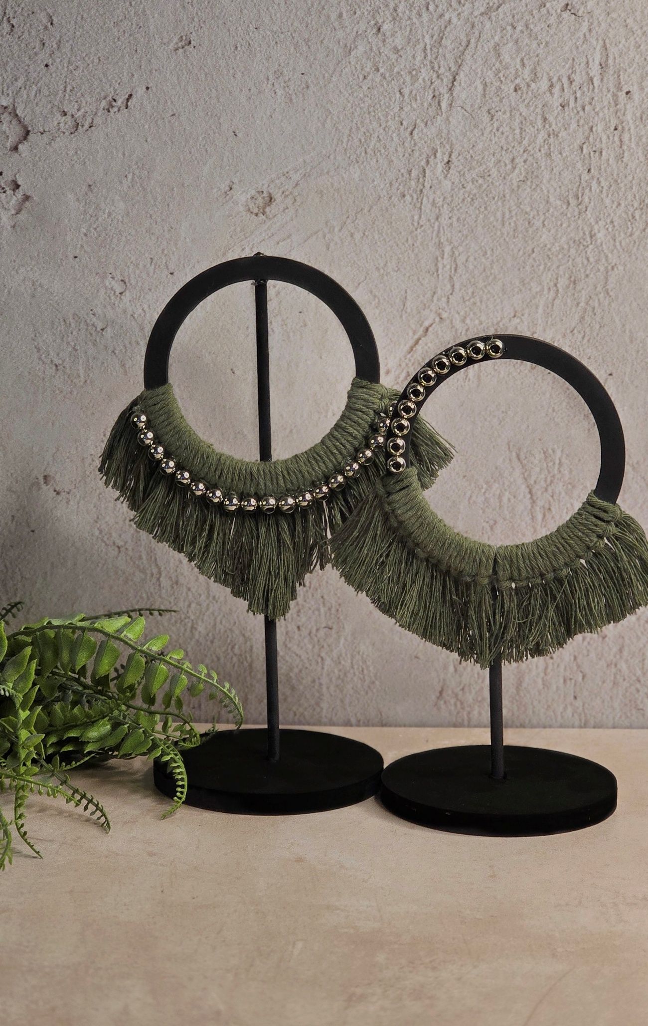 Dos collares de aro con flecos de color verde oliva sobre soportes negros.